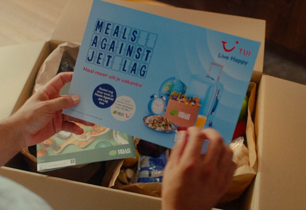 A person holding a card that reads "Meals against jet lag" above an open shipment box